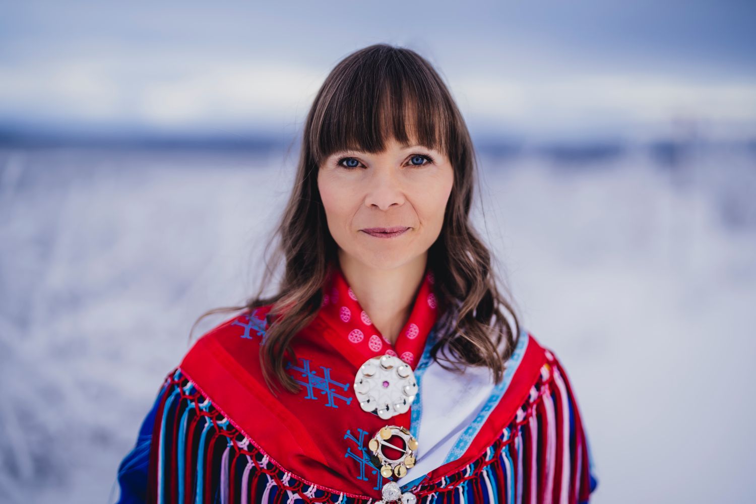 Ann-Helén Laestadius stands in traditional Sámi attire in front of snowy backdrop.