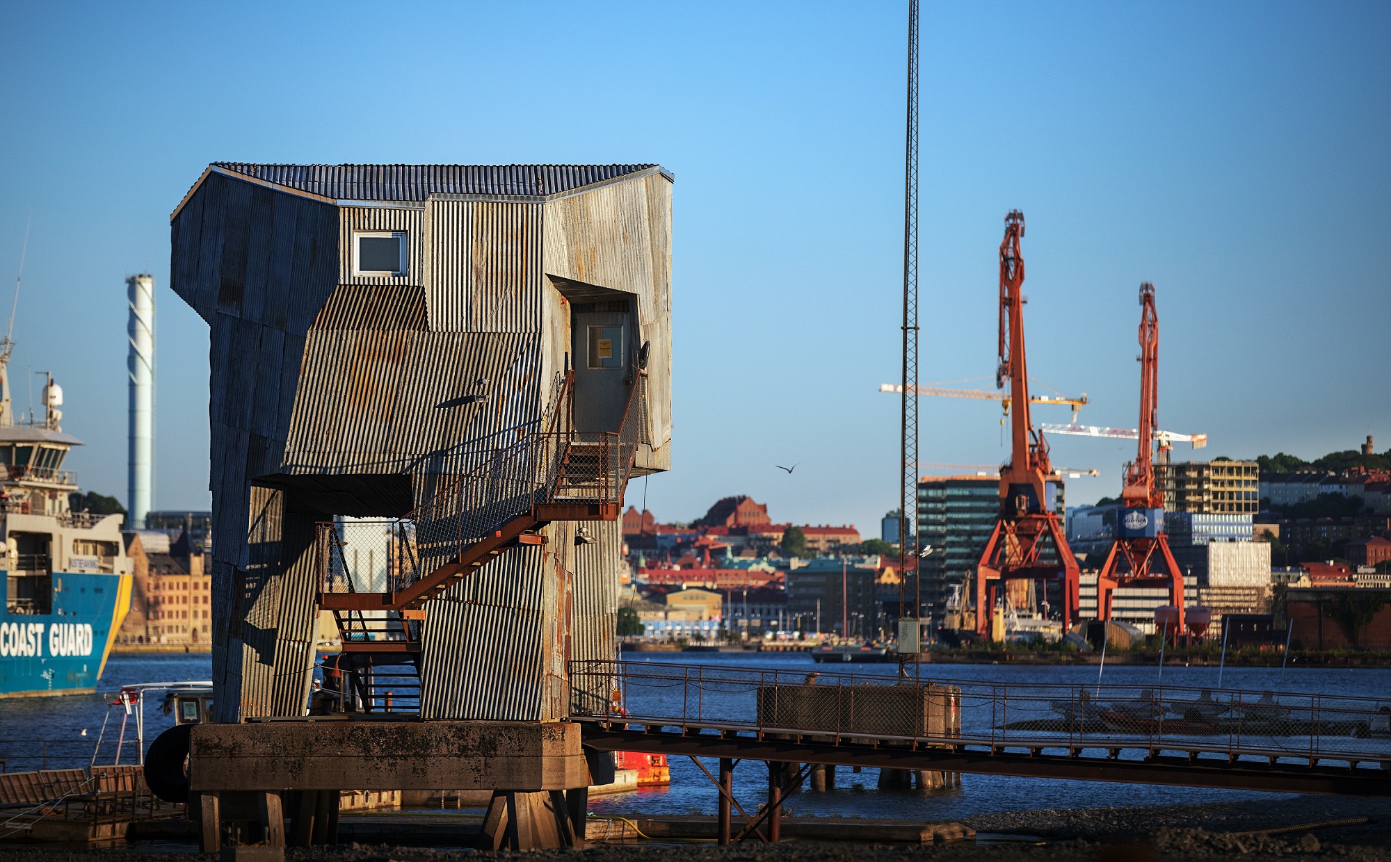 A tall, corrugated iron office looks out over red cranes in Gothenburg's port.