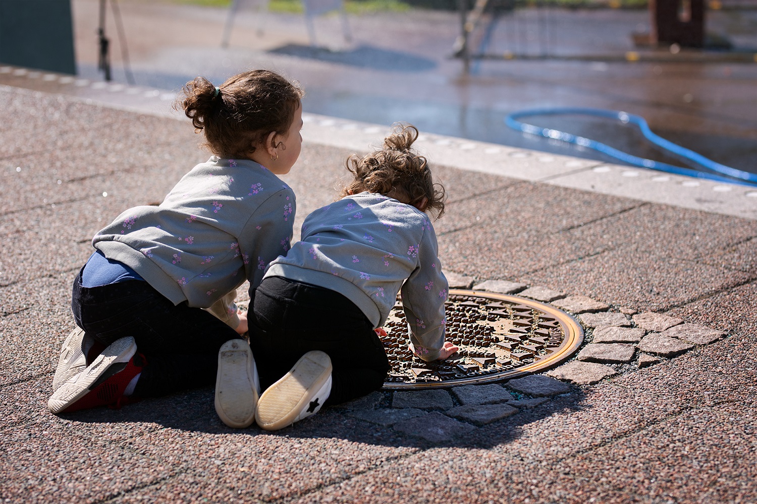two young children reading manhole covers on a sunny city day.