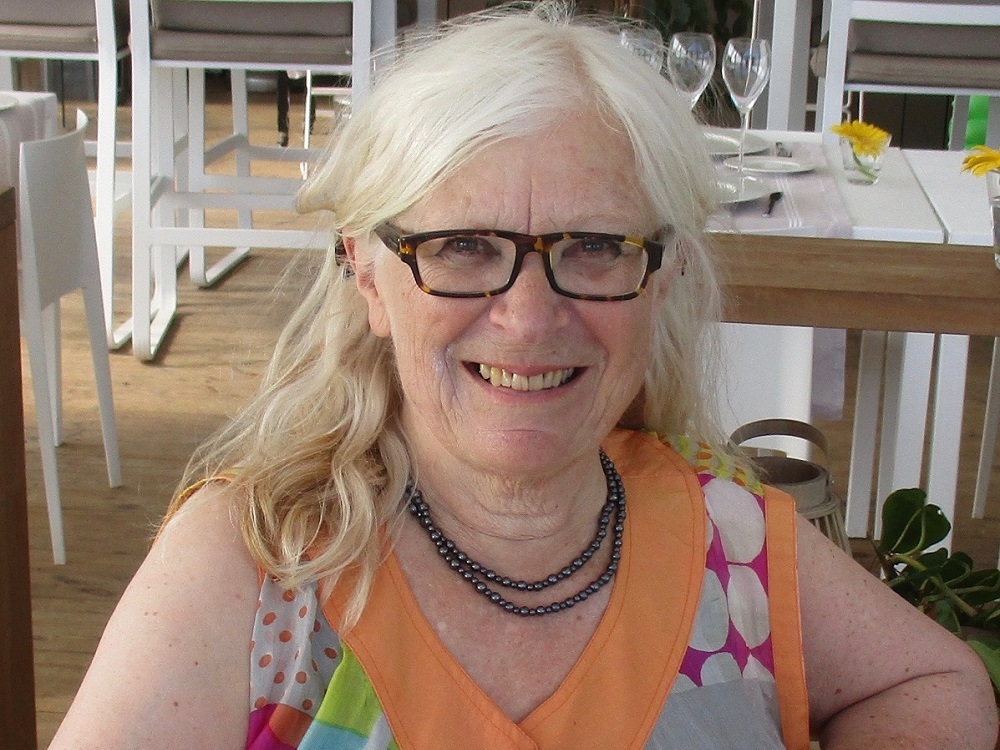 Eivor Martinus smiles at the camera, sitting in a relaxed pose wearing a colourful summer blouse.