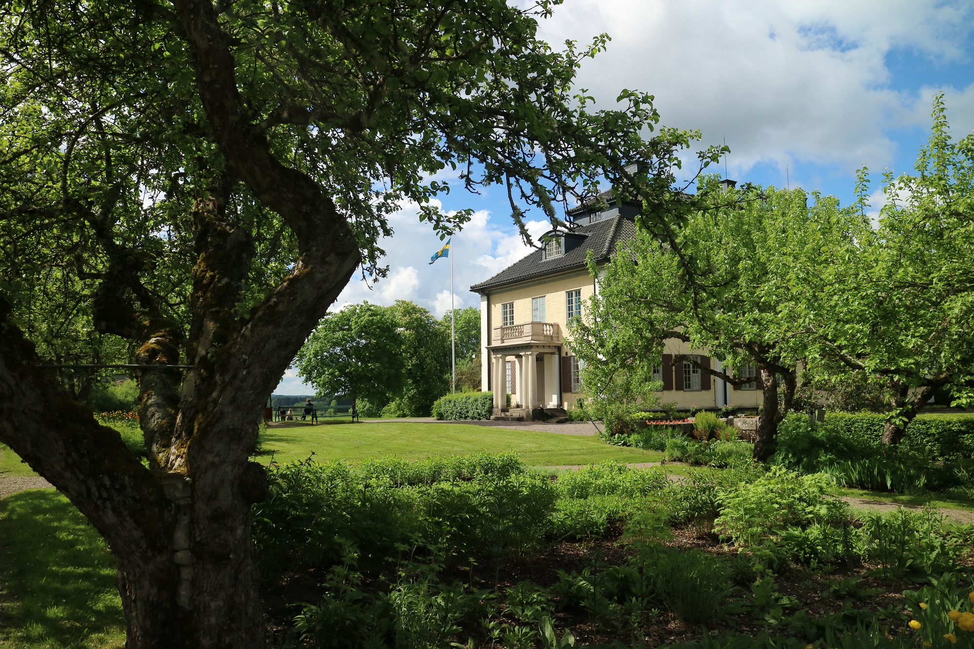 Yellow manor house seen through a verdant garden.