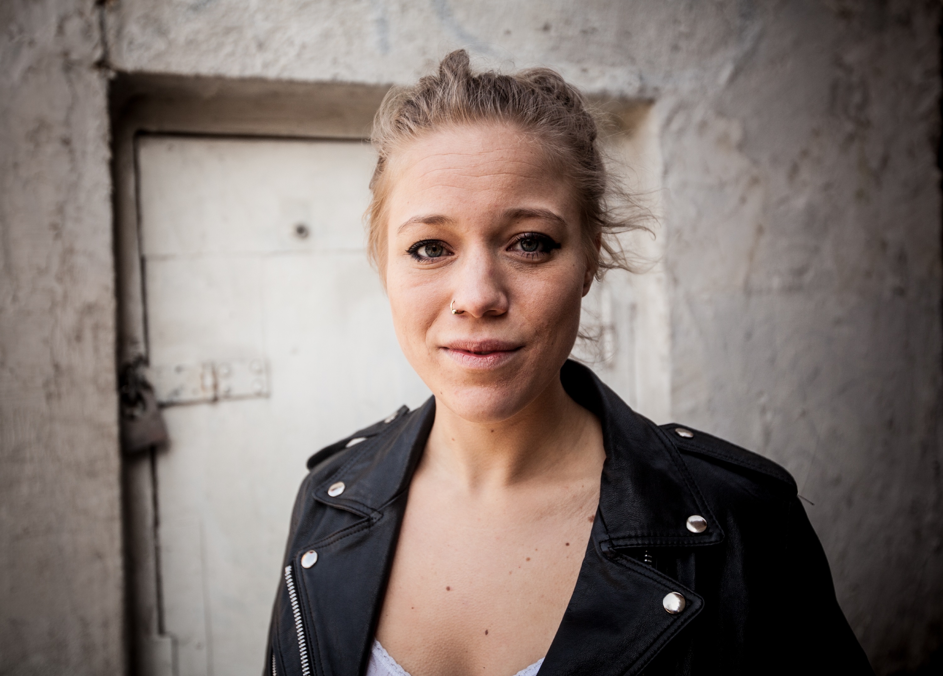 Blonde woman with hair tied back, nose piercing and leather jacket