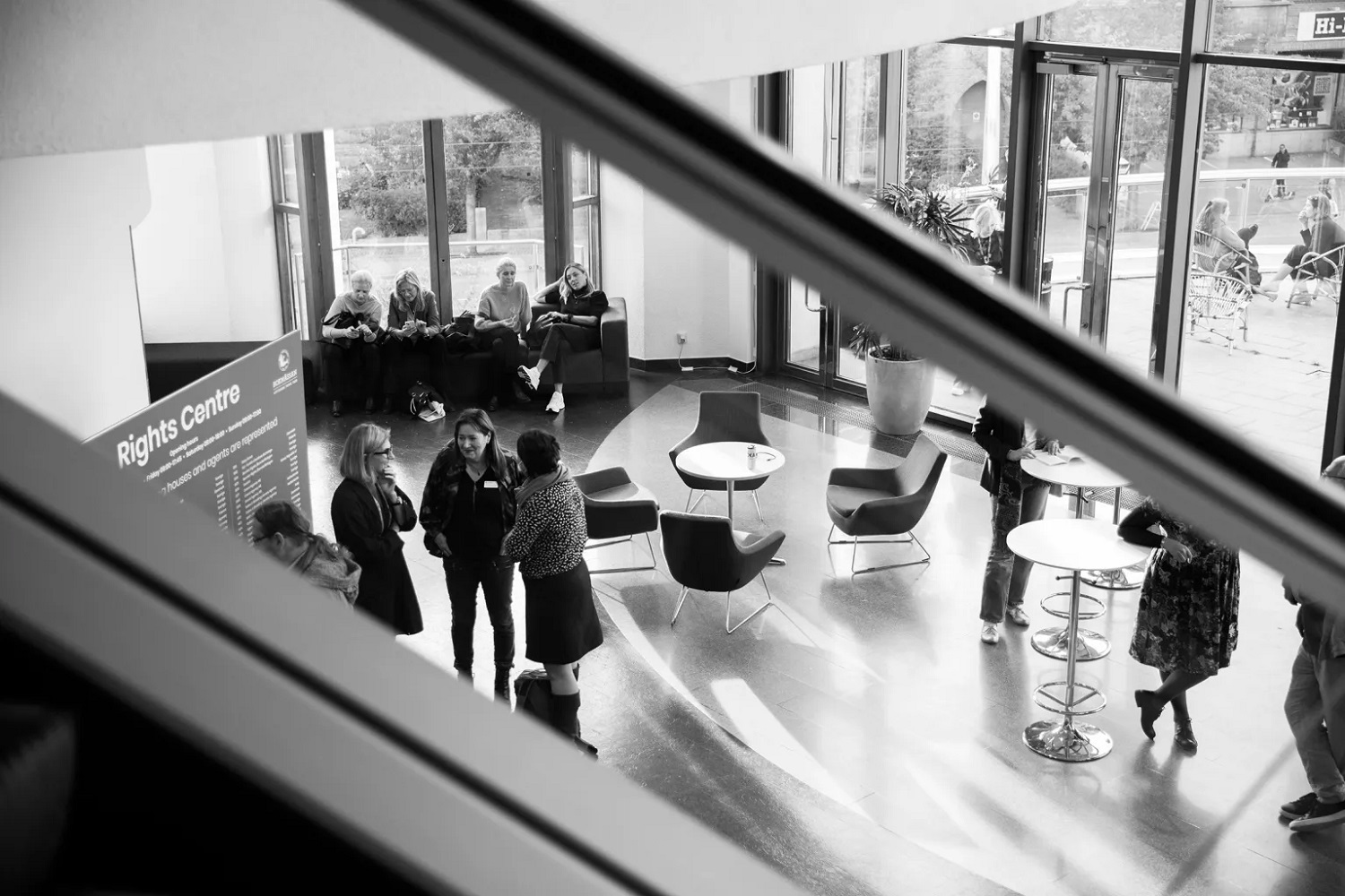 Three women talk in foyer with empty chairs and tables.