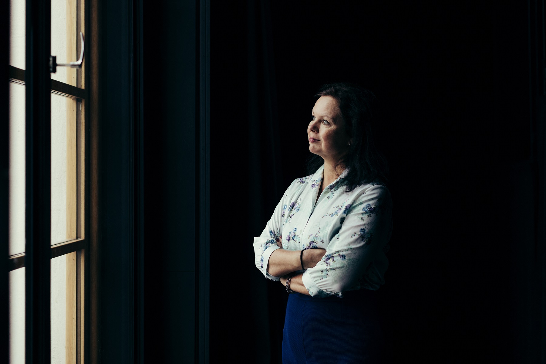 Ann-Luise Bertell gazing through window in dramatic lighting.