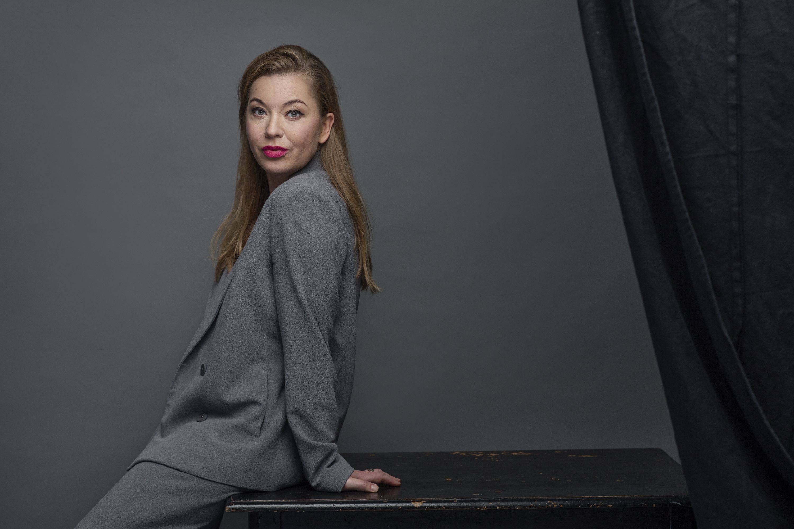 Karolina Ramqvist sitting sideways on table in grey suit
