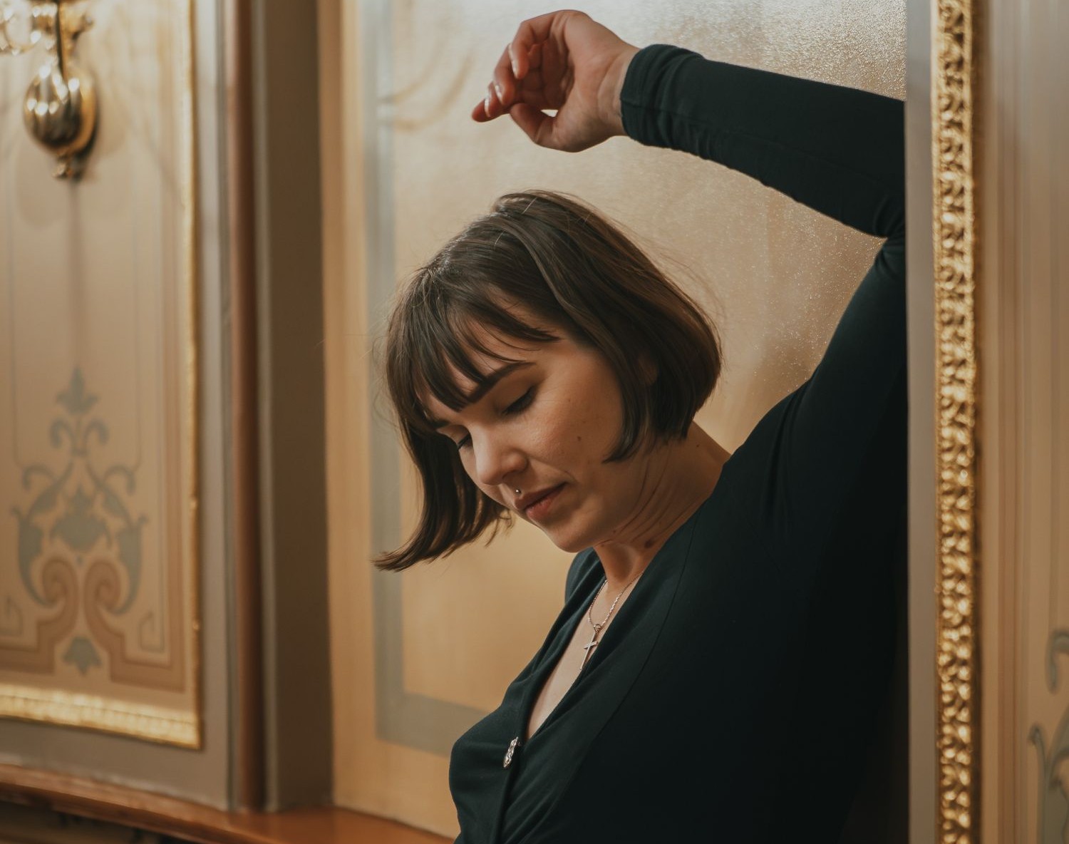 Lyra Ekström Lindbäck leans against ornately decorated wall with her arm raised over her head.