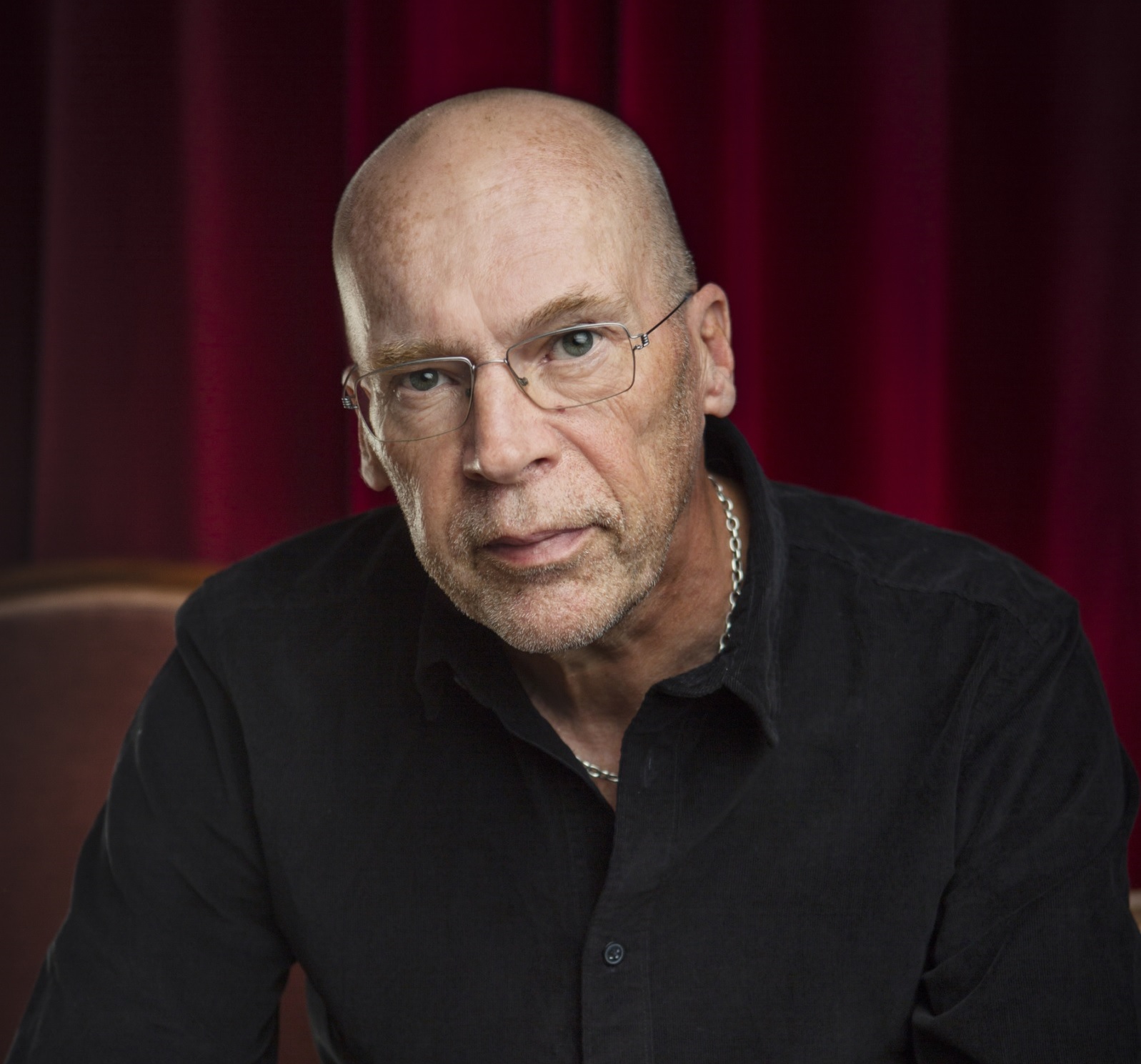 Robert Åsbacka leaning forward in black shirt, in front of a red background