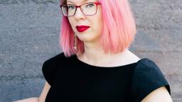 Maria Turtschaninoff with pink hair and red glasses by grey wall