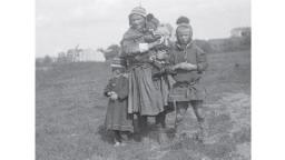 Archive image of a Sámi woman with a baby in her arms and two children standing next to her