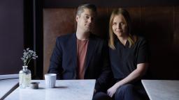 A man and a woman sitting on a leather restaurant bench by marble tables