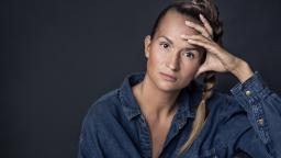 Woman with hair in ponytail holding her hand to her forehead.