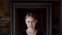 Smiling woman stands in front of dark picture frame