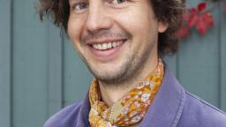 Smiling man with brown hair in yellow scarf and purple jacket