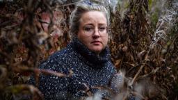 Woman with glasses wearing polo-neck jumper in bushes