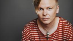 Man with blond hair in side parting and skeleton necklace.