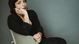 Woman with short brown hair and black cardigan sitting side-on in chair