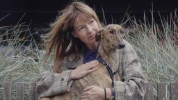 Woman in chequered coat sitting with dog on her lap gazing into distance