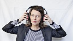 Woman with shoulder-length, light-brown hair wearing a blazer and stripy top holding headphones over her ears
