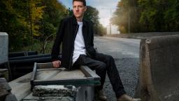 Mikael Yvesand sitting on road barrier in black jacket.