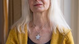 Inger Edelfeldt looks at camera wearing a yellow cardigan and star pendant.