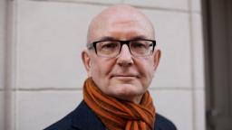 Peter Kadhammar looks at camera wearing orange scarf and glasses.