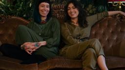Amanda and Sofia Chanfreau sitting on a sofa, smiling, in green jumpsuits.