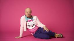 Jonas gardell in kitty shirt sitting in front of a pink background
