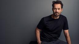 Jens Liljestrand in black t-shirt sitting on stool in front of grey background.