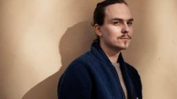 Mattias Timander in blue jacket standing in front of cream wall
