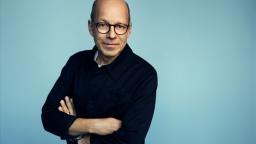 Author portrait of Augustin Erba in front of blue background