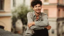 Oskar Kroon sitting in urban environment with arms around his knees.