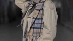 Therese Bohman standing in trenchcoat holding the back of her head.