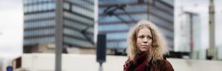 Blonde woman standing in front of tower blocks in red scarf