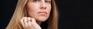 Young woman with long blond hair and blue eyes against black background.