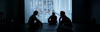 three men sitting in a darkened room with a projection in the background.