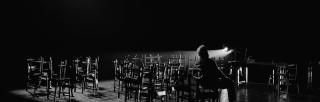 black and white photo of man sitting among chairs on a stage